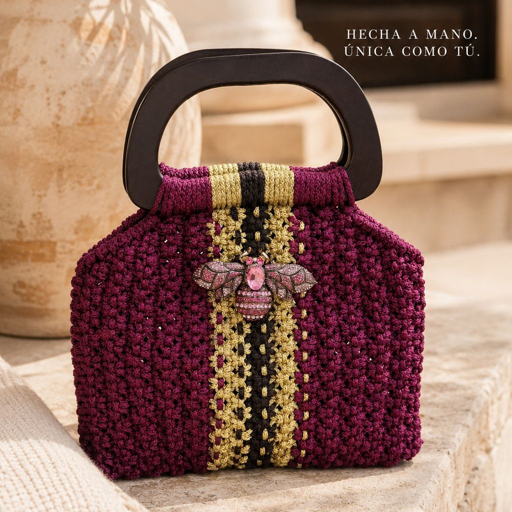Cartera Marroc de Lukkbags tejida a mano en macramé burdeo con franja dorada y negra, asa rígida de madera y broche joya rosa