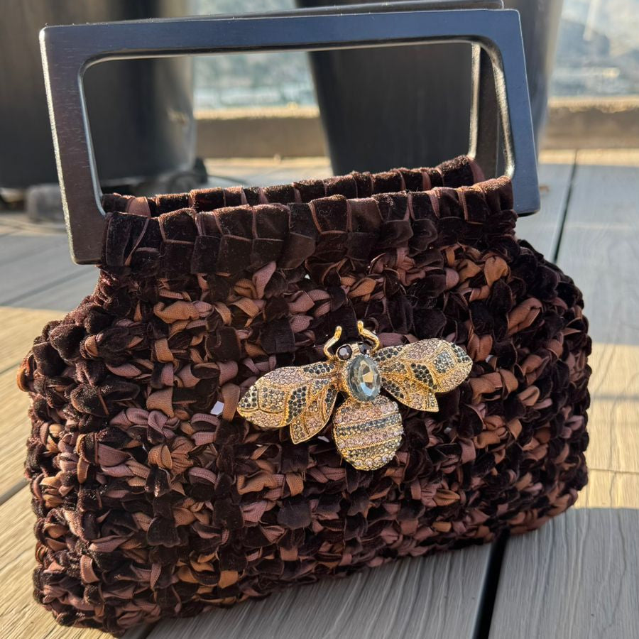 Cartera Velvet Lukkbags tejida a mano en terciopelo chocolate con asa rectangular de madera negra y broche abeja con cristales dorados