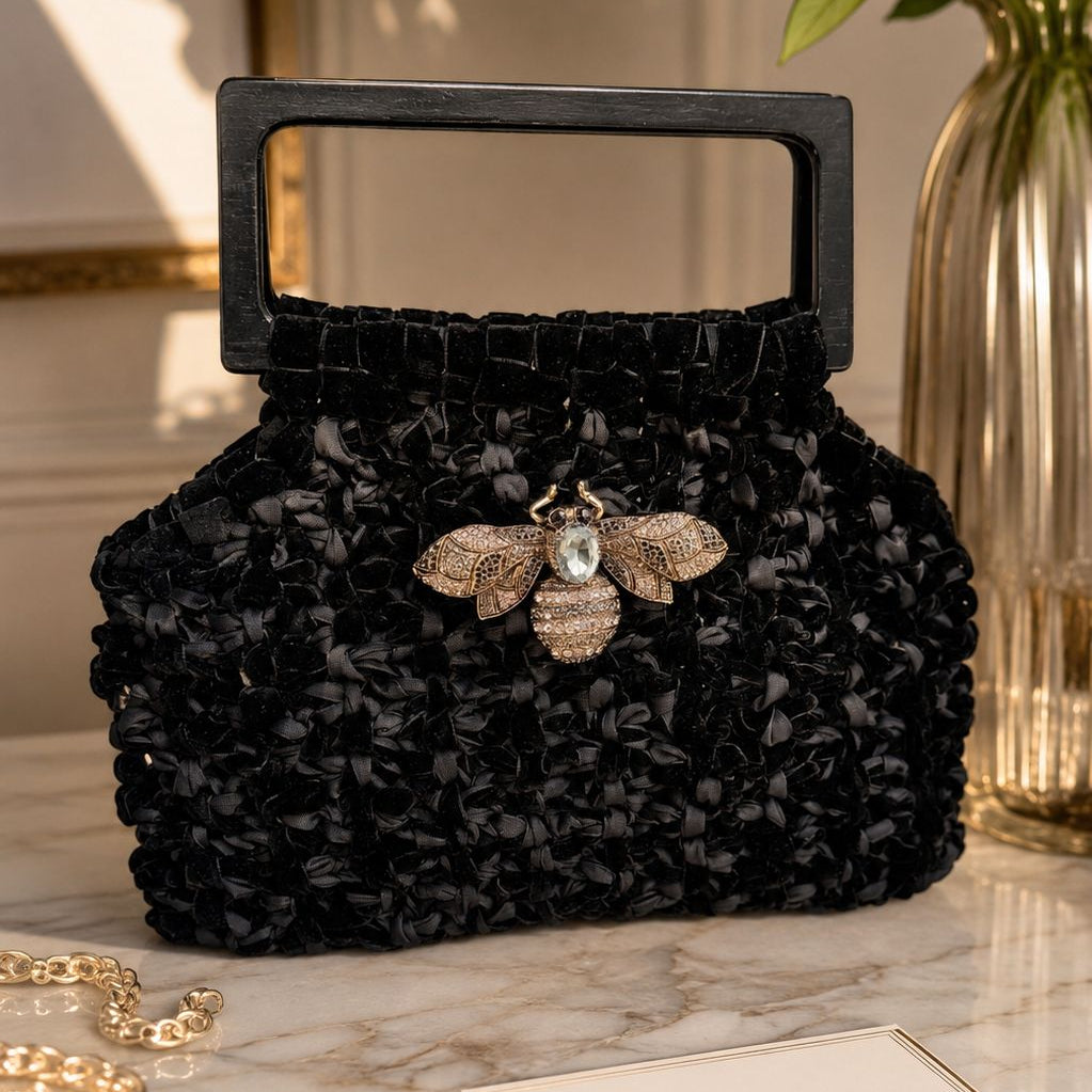 Cartera Velvet Lukkbags tejida a mano en terciopelo negro con asa rectangular de madera y broche abeja con cristal