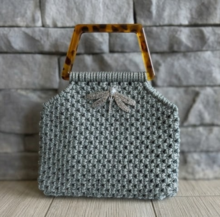 Cartera Zaya Lukkbags tejida a mano en macramé gris con asa cuadrada efecto carey y broche libélula plateado